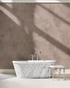 a bathroom with a marble bathtub next to a stool on the floor in front of a wall