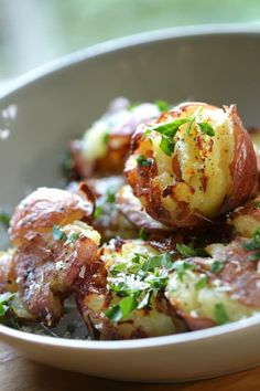 a white bowl filled with potatoes covered in parmesan cheese and garnished with herbs