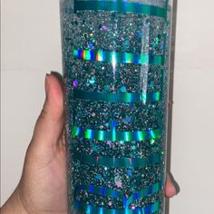 a hand holding up a blue and green glittered tumbler with ribbons on it