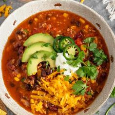 a white bowl filled with chili, cheese and avocado on top of a table