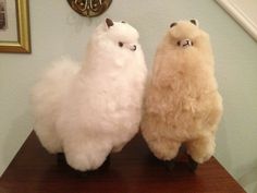 two stuffed llamas sitting on top of a wooden table next to each other