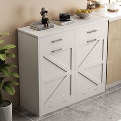 a white cabinet sitting next to a potted plant and a bowl of fruit on top of it