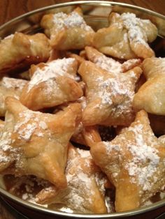 a metal bowl filled with pastries covered in powdered sugar on top of a wooden table