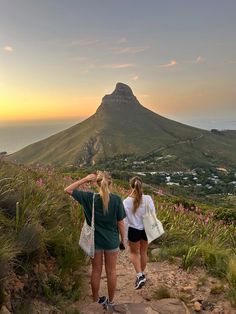 two young women walking up a hill towards the ocean with mountains in the back ground