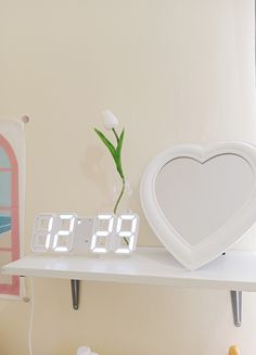 a white clock sitting on top of a shelf next to a vase filled with flowers