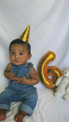 a baby sitting next to a number six balloon and a teddy bear wearing a party hat