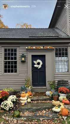 a gray house with pumpkins and other decorations on the front porch, along with fall foliage