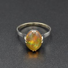 "A rainbow is swimming in this gorgeous antique opal ring! A beautifully proportioned opal cabochon is centered with cardinal prongs (north, south, west and east) in an 18k white gold setting. The opal features a transparent orange body, typical of Mexican jelly opals, with a \"contra luz\" color flash seen when the gem interacts with light. The color play is astounding, with every color of the rainbow ignited within the body of the opal, having painterly brush-stroke like patterns. This ring hails from the 1920s and has been tenderly well-cared for in its lifetime. It is in wonderful condition and ready for a new owner. This ring could be a perfect alternative engagement ring, gift for someone with an October birthstone or simply a present for an antique jewelry lover.   Opal is a fascina Classic Cabochon Opal Ring, Classic Ethiopian Opal Gemstone Rings, Formal Opal Ring With Polished Finish, Antique Opal Jewelry In Yellow Gold, Classic Opal Jewelry With Polished Finish, Classic Yellow Gold Opal Ring, Classic Oval Opal Ring With Polished Finish, Formal Yellow Gold Ethiopian Opal Ring, Fine Jewelry Oval Cabochon Opal Ring