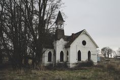 a man pointing at an old white church in the middle of a field with trees