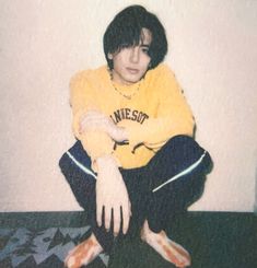 a young person sitting on the floor with their legs crossed and wearing a yellow shirt