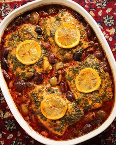 a casserole dish with lemons, olives and meat in it on a rug