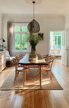 a dining room table with chairs and a vase on it's centerpiece, in front of a large window