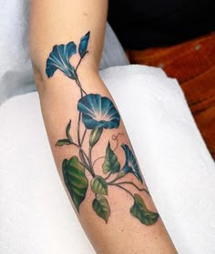 a woman's arm with a blue flower and leaves tattoo on her left arm