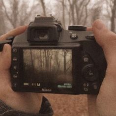 a person holding up a camera in front of trees