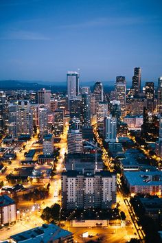 an aerial view of a city at night with lights on and buildings in the foreground