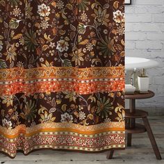 a shower curtain with an orange and brown floral design on it's side next to a white bathtub