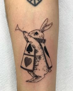 a rabbit with a coat and playing cards tattoo on the leg is shown in black ink