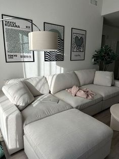 a living room with white couches and pictures on the wall above them, along with a large ottoman