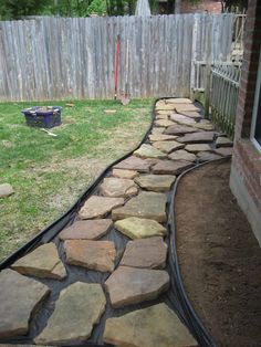 a stone path in the backyard leading to a fenced in area with grass and rocks