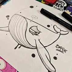 some markers and pens are laying on top of a drawing book with an image of a whale