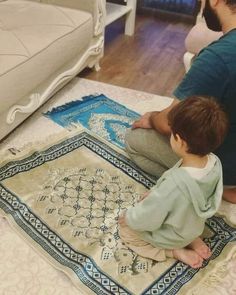 a man sitting on the floor next to a child who is playing with a rug