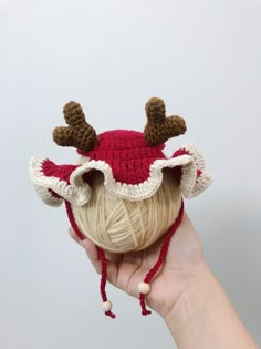 a hand holding a ball of yarn with reindeer antlers on it's head