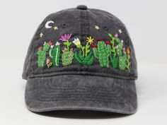 a gray hat with embroidered cactus and flowers on the front, sitting against a white background