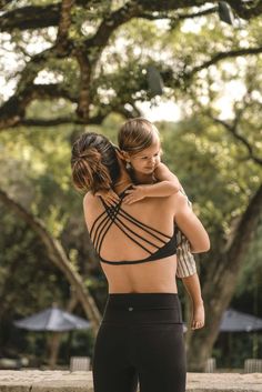 a woman in black sports bra and leggings hugging another woman's back