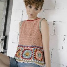 a woman is sitting on the floor wearing shorts and a crocheted top with an open back