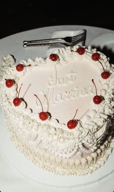 a heart - shaped cake with cherries on it is sitting on a plate next to a fork and knife