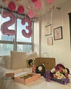 balloons are hanging from the ceiling in front of a couch with flowers and gifts on it