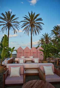 an outdoor seating area with palm trees in the background and pink striped cushions on it