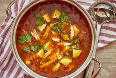 a bowl of soup with meat, potatoes and cilantro on a striped napkin