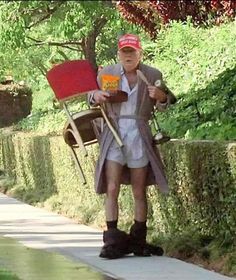 a man walking down a sidewalk with a red chair on his back and a broom in his hand