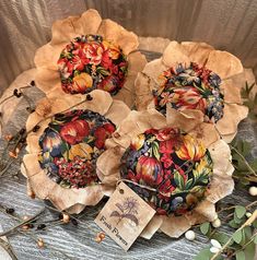 three decorative paper flowers sitting on top of a wooden table next to leaves and berries