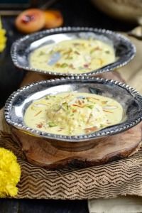 two metal bowls filled with food on top of a wooden table next to yellow flowers