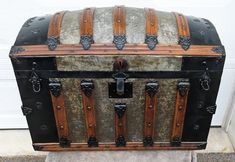 an old trunk is sitting outside on the concrete near a garage door, with metal latches and wood trimmings