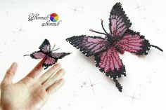 two pink and black butterflies are being held up by someone's hand on a white surface