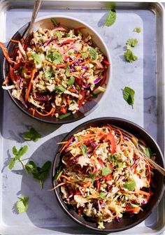 two bowls filled with coleslaw and carrots sitting on top of a metal tray