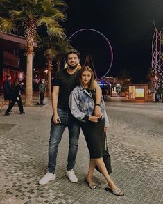 a man and woman standing next to each other in front of palm trees at night