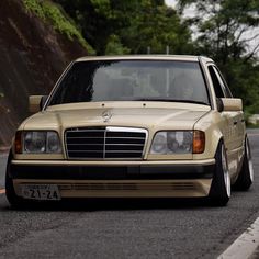 a beige mercedes benz is parked on the side of the road with trees in the background