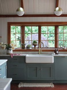 a kitchen with wooden floors and green cabinets, white counter tops and two large windows