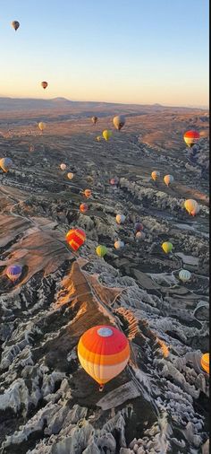 many hot air balloons are flying in the sky over rocks and mountains at sunrise or sunset