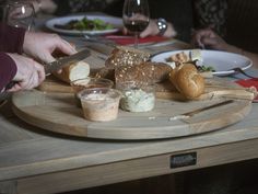 people are sitting at a table with bread and other food on the plate, while one person holds a knife in their hand