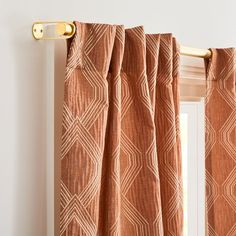 an orange curtain hanging on the side of a white wall next to a window with gold hardware