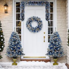 a front door decorated for christmas with blue wreaths and trees in the snow next to it