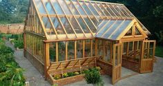 a large wooden greenhouse with many windows and plants in the garden area next to it