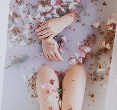 a woman's legs are covered in flowers and petals as she lays on the floor