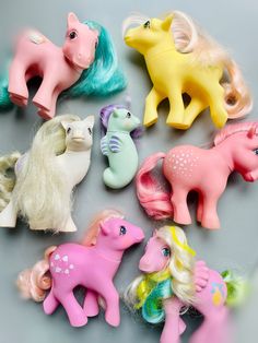 many different types of toy ponys on a table with grey background and one has blonde hair