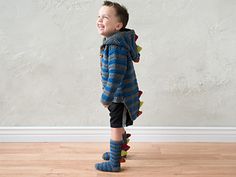 a young boy standing on top of a hard wood floor next to a white wall